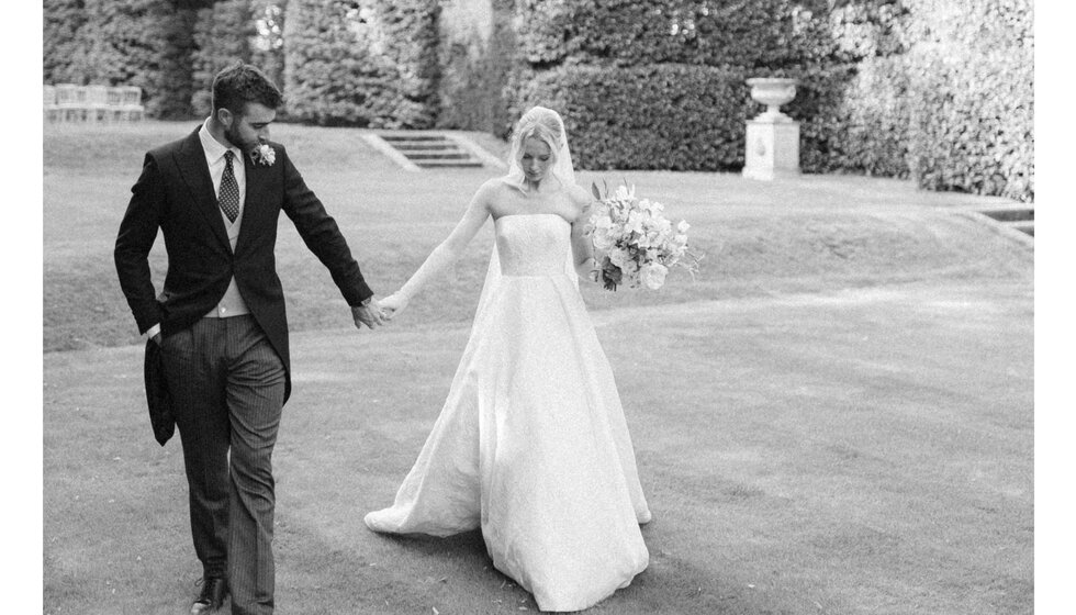 A groom and bride stroll through the garden of their Hampshire country house wedding venue.