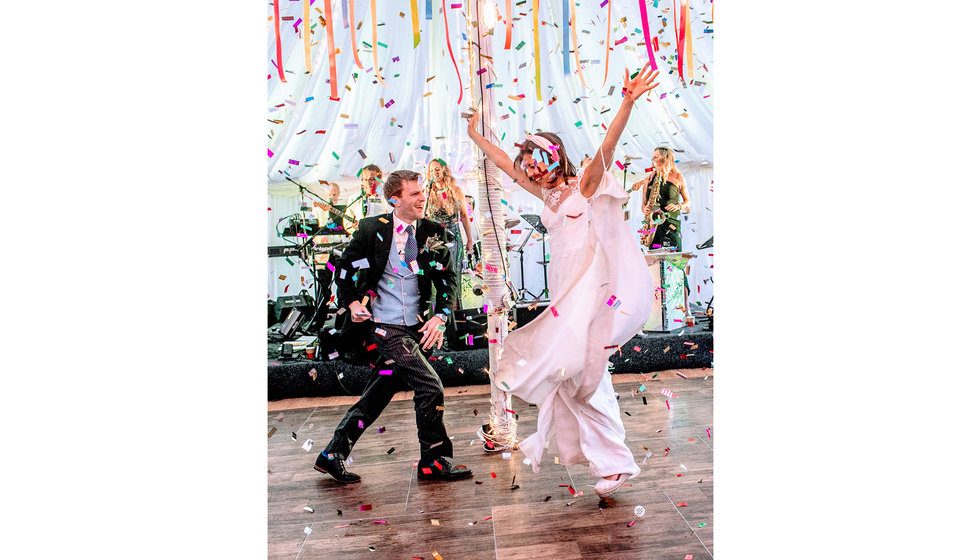 The bride and group dancing energetically with colourful confetti all around them.