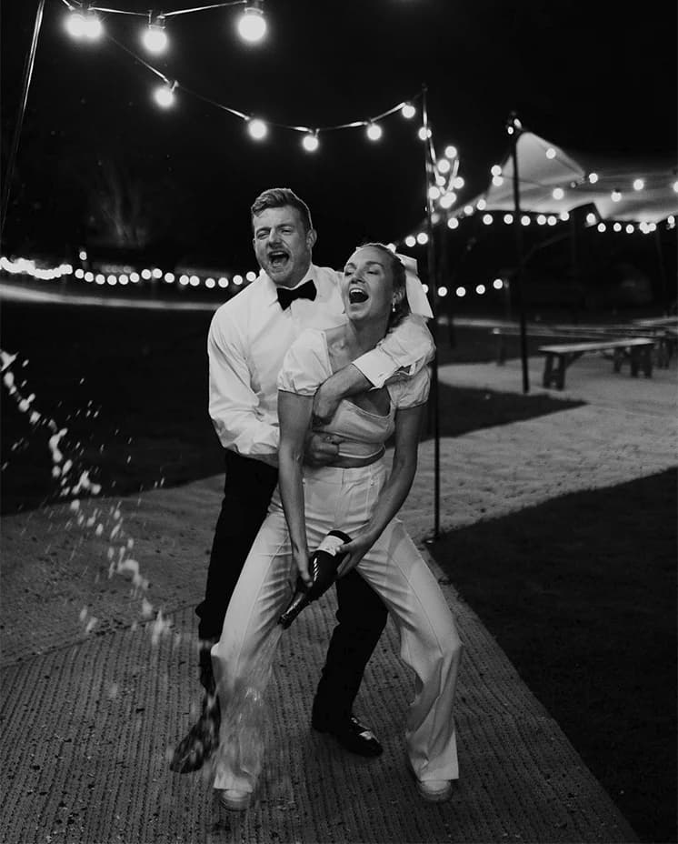 Bride and groom celebrate their wedding spraying champagne outside their wedding marquee/