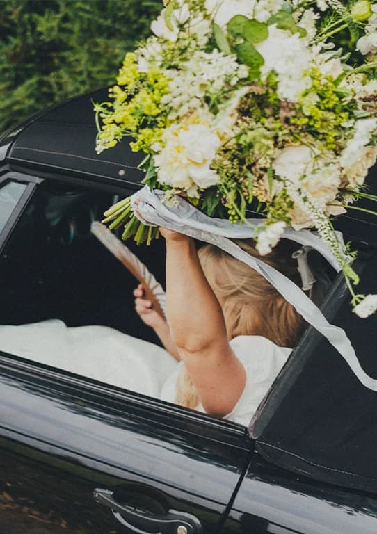 The Wedding Present Company brides wave with flower bouquet while sitting in a vintage car.