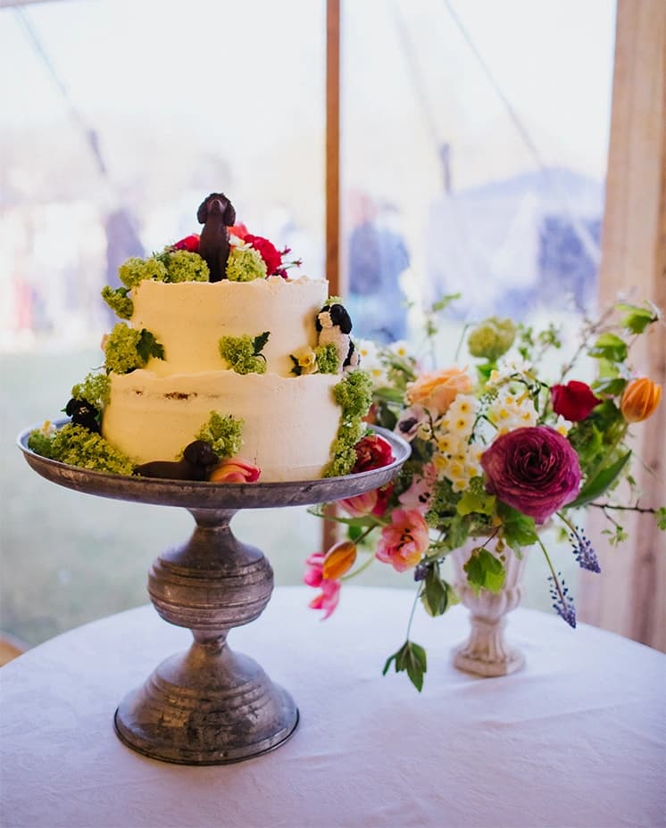Two tier wedding cake decorated with flowers and dogs displayed next to a matching floral bouquet