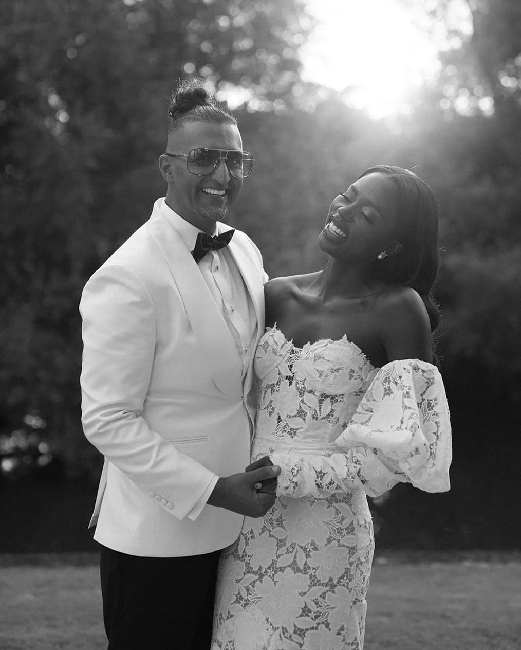 Groom in white tux and bride wearing lace dress are laughing
