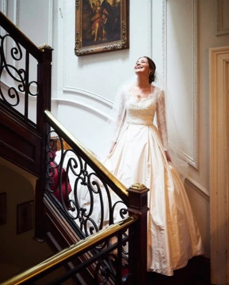 Smiling bride standing on a grand staircase wearing a traditional wedding dress