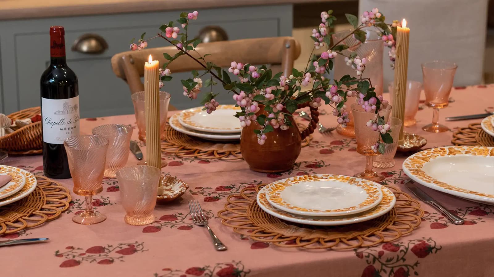 A cosy autumn tablescape with handpainted yellow plates, coloured glassware, candles and flowers on a pink embroidered tablecloth