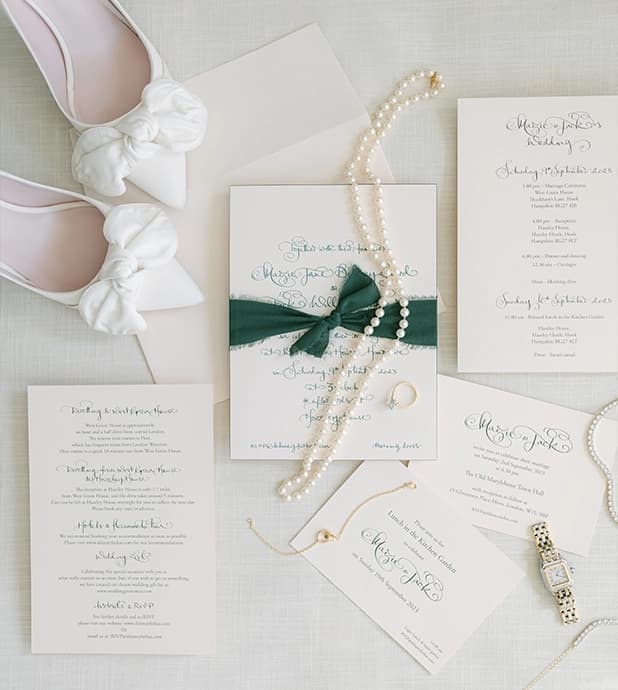 Wedding jewellery and shoe placed on a timeless handwritten wedding stationery with bow.