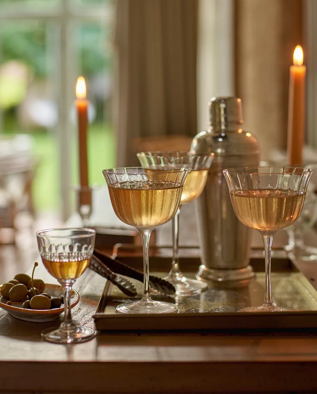 A tray with wedding presents for cocktails lovers features martini in cocktail coupe glasses next to a cocktail shaker.