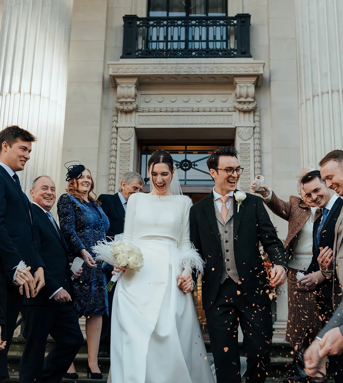Bride and groom leave their wedding ceremony in townhall while guests are throwing confetti