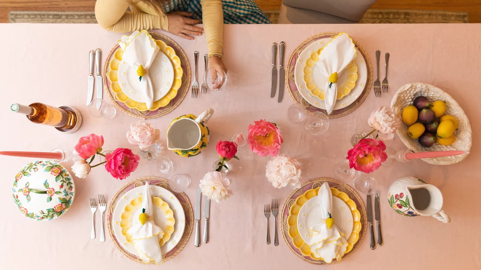 A person sits next to a table set for four people with a pink and yellow Italian inspired tablescape featuring tableware wedding gifts. 
