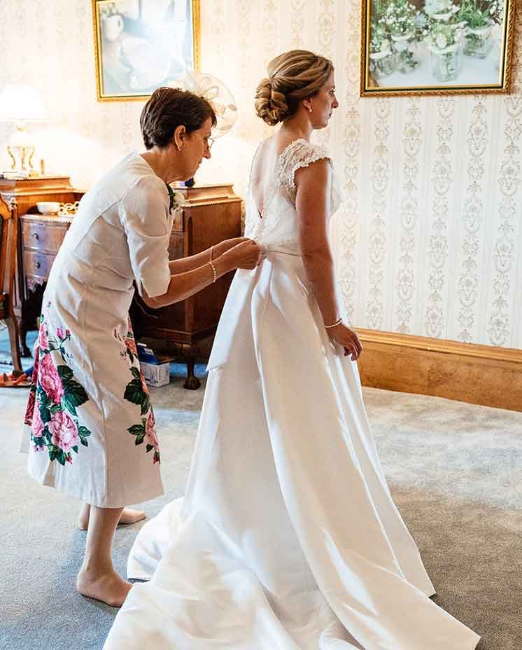 Mother of the bride helping bride put on her dress