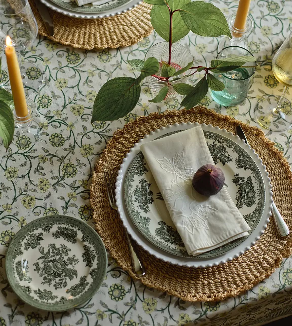 A beautiful tablesetting with floral tablescape, rattan placemats and ornamental dinner plates. 