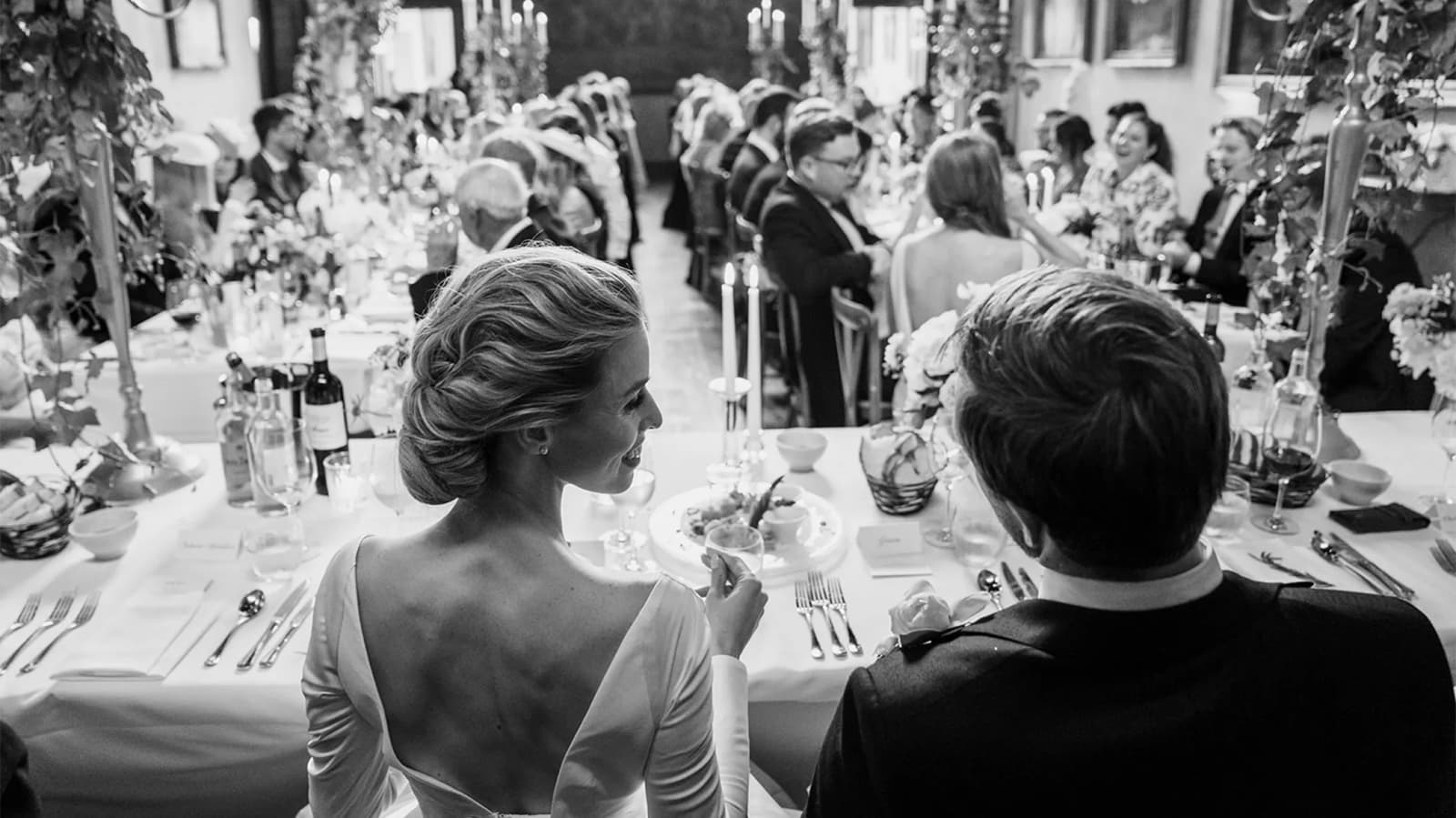 Bride and groom sit behind the top table, looking at their guests
