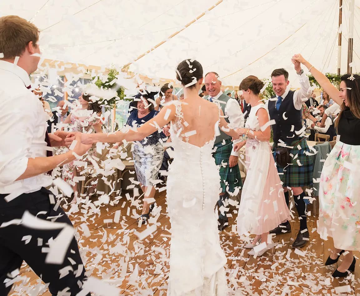 Guests joins bride and groom during their first dance in marquee, celebrating with confetti.