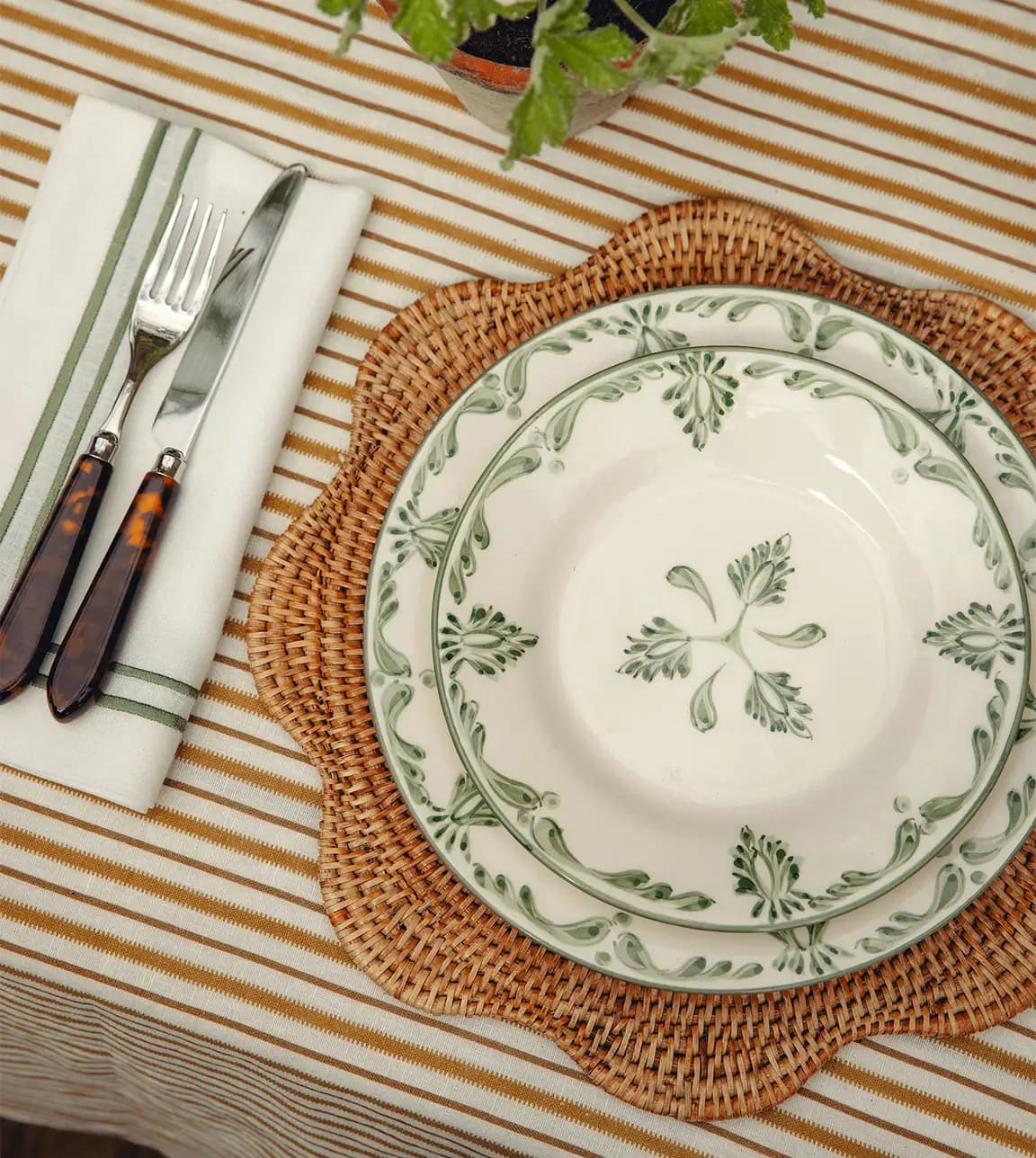 Summer tablescape features Rebecca Udall plate with green pattern, placed on rattan placemat