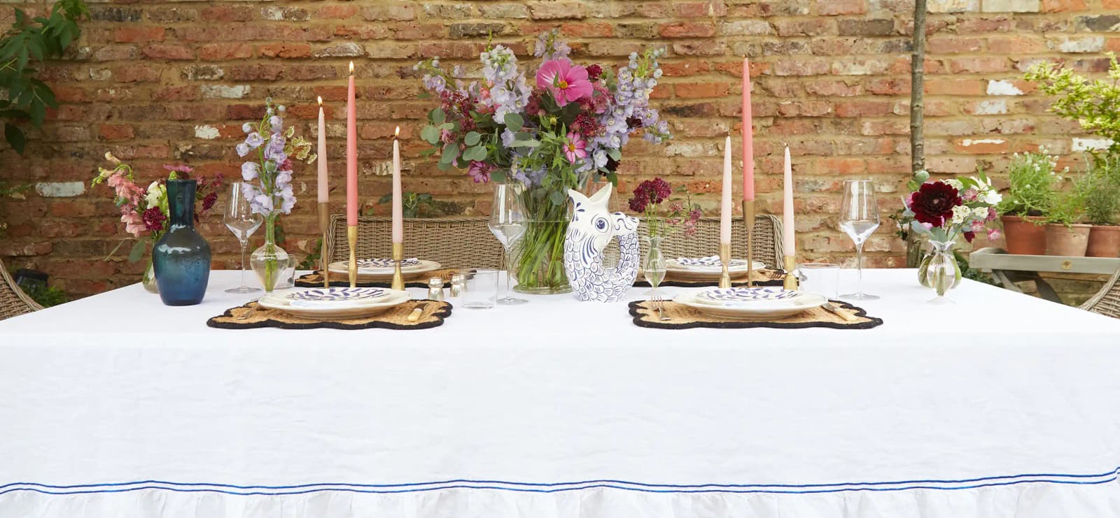 Purple & blue tablescape features tableware wedding presents: brass candles, white tablecloth with a stripe, gluggle jug, flowers and plates