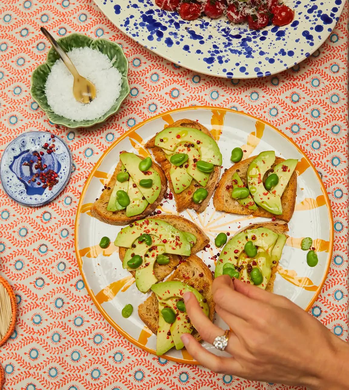 A hand with engagement ring takes food from the handpainted platters gifted as the wedding present.