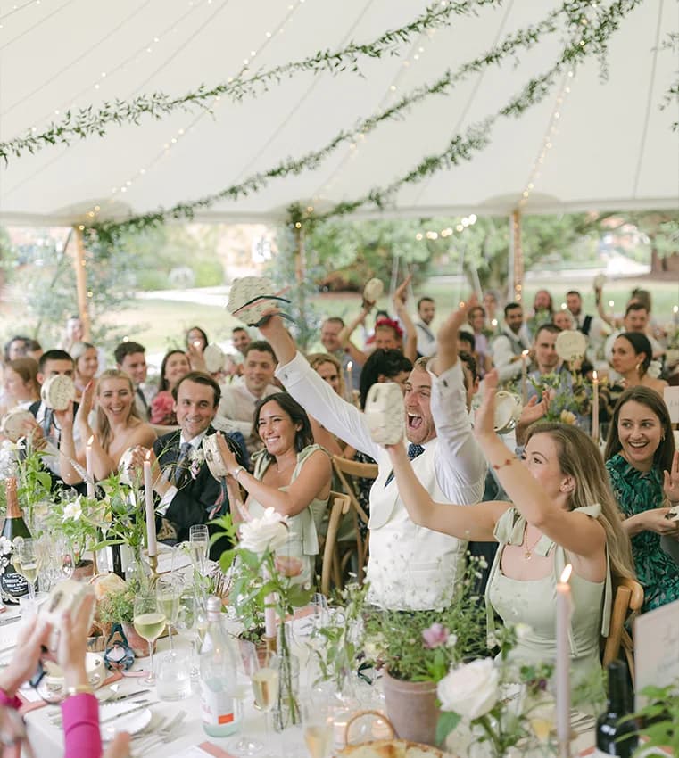 Wedding guests in a traditional marquee cheers with bespoke tambourines.