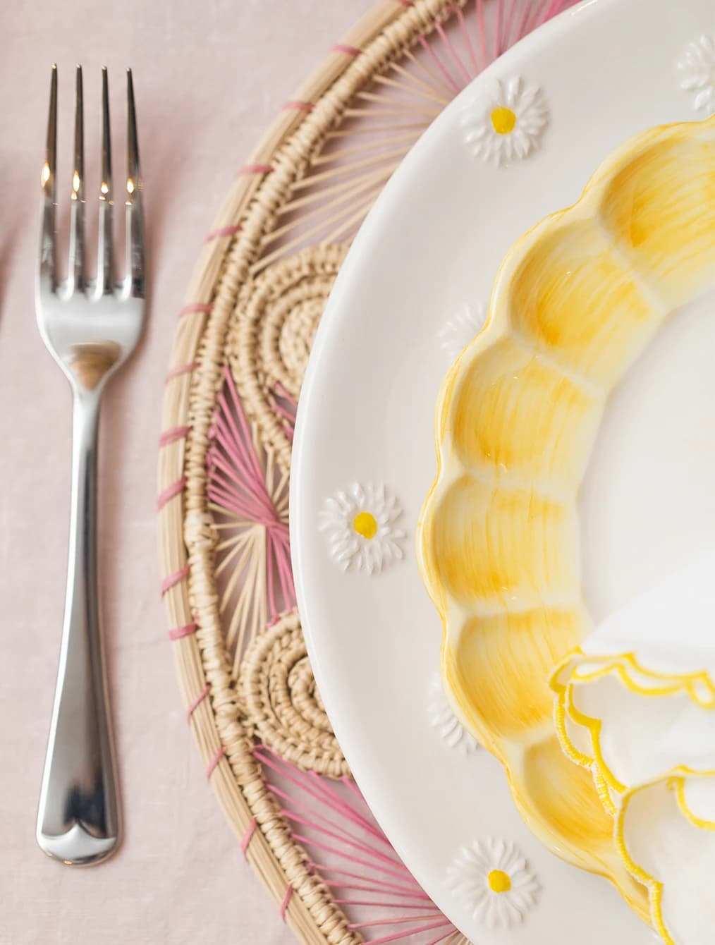 A mix of hanpdainted ceramic plates from Skye McAlpine Tavola is placed on a rattan placemat.