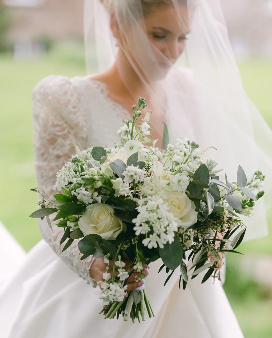 English bride in embroidered dress and veil holds flower bouquet before her wedding ceremony.