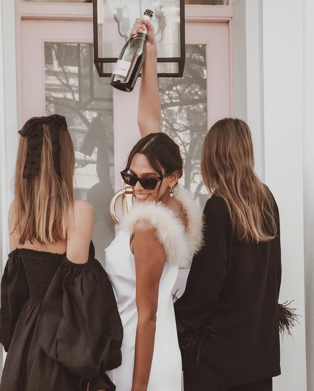 A bride with friends in party dresses celebrates her hend do with a bottle of champagne.