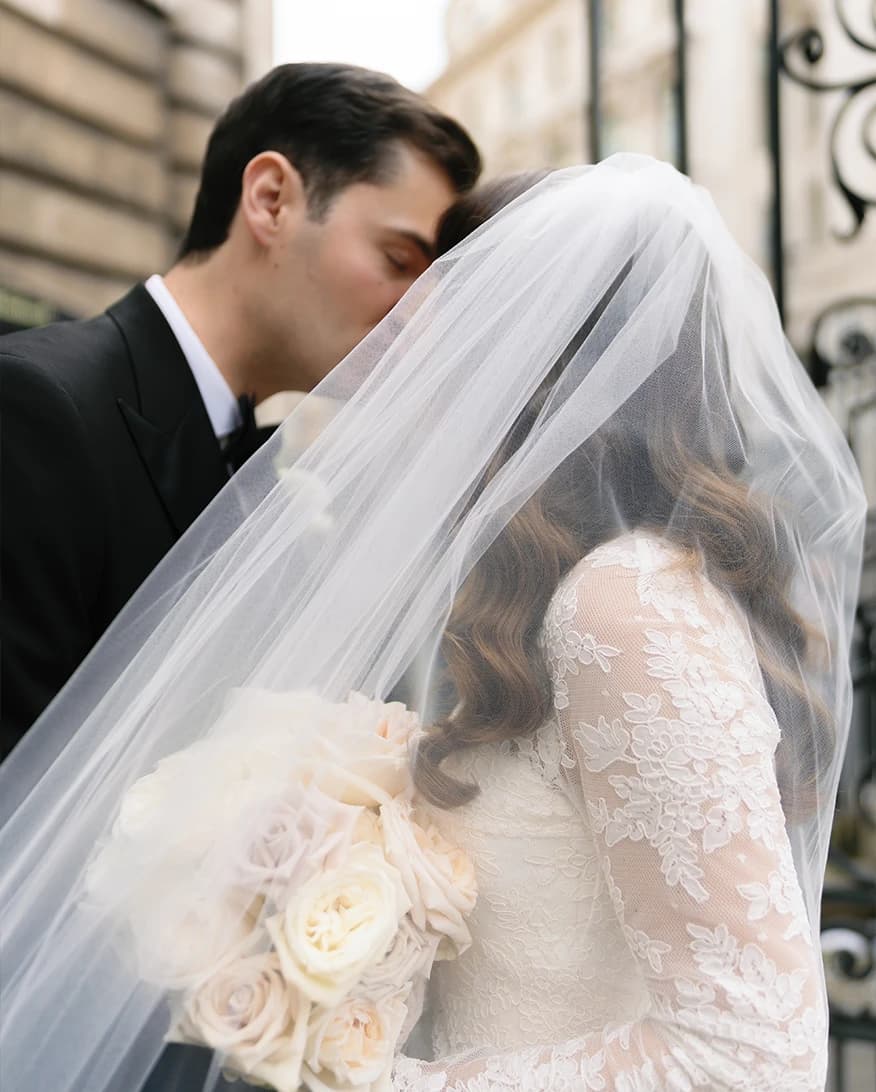 Bride and groom are kissing while being slightly covered with bride's veil