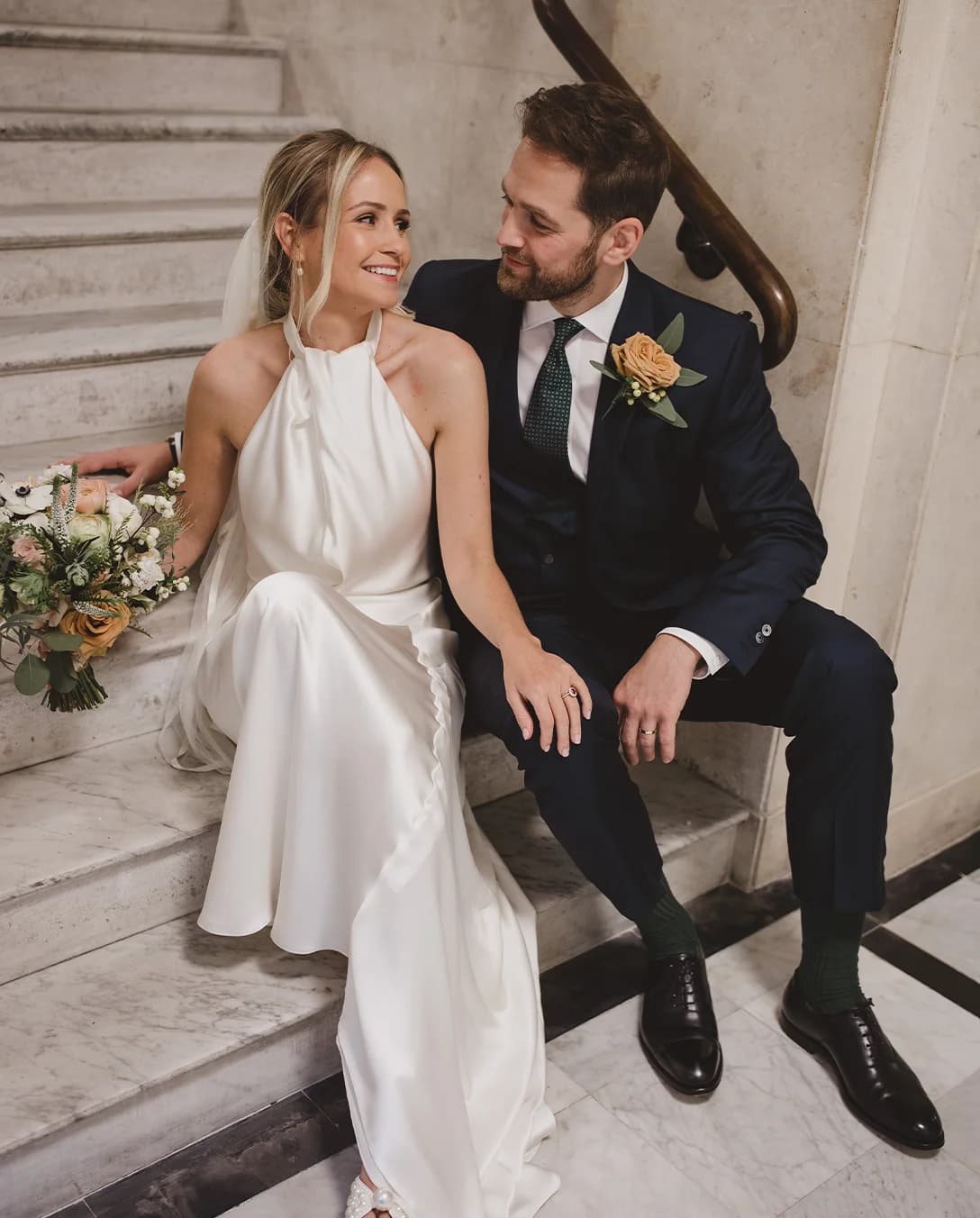 Husband and wife smiling posing on marble stairs at their reception venue