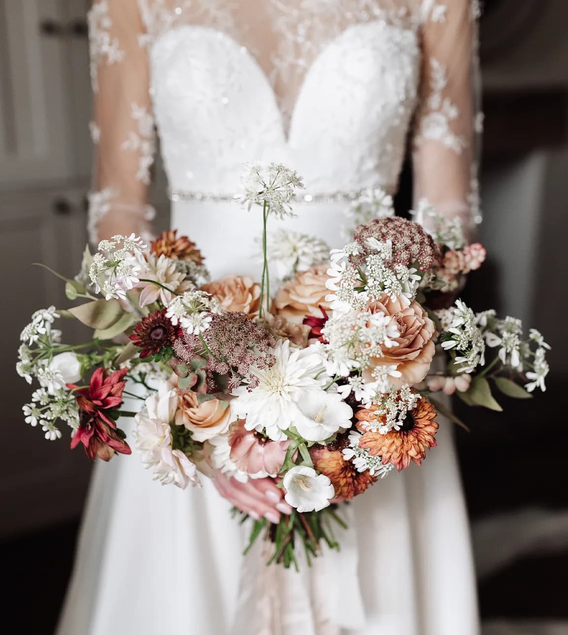 Bride in lace wedding dress holds autumn wedding flower bouquet