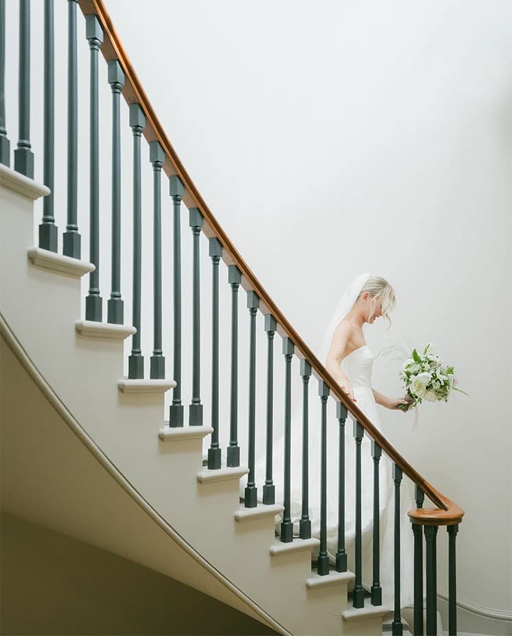 A brides walks down the spiral staircase in her stunning Sassi Holfrod strapless dress and veil