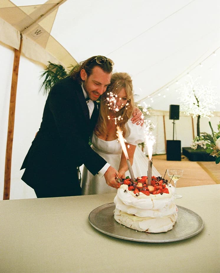 Bride and groom cutting their wedding pavlova decorated with summer fruits and sparklers