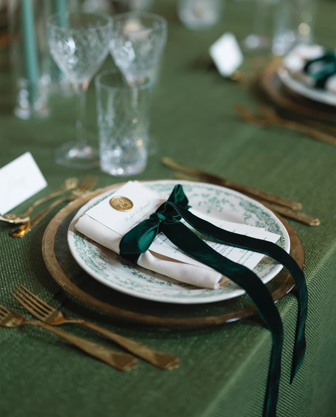 White and green wedding table decor with floral themed plates and green velvet bow.