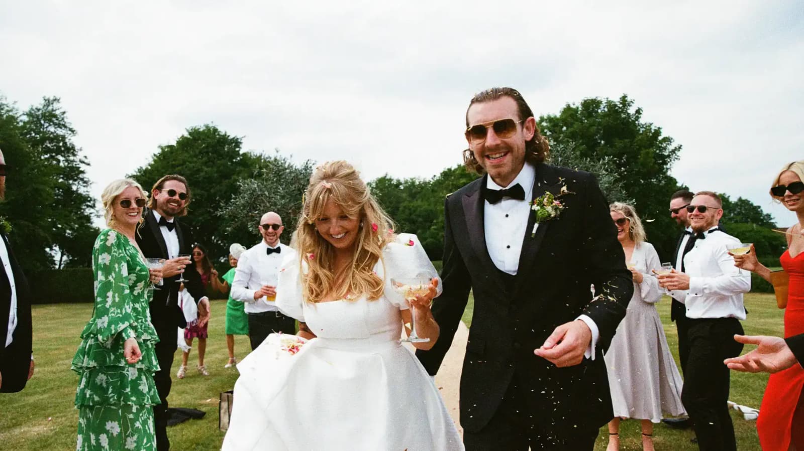 bride and groom smiling and walking down path with guests throwing confetti