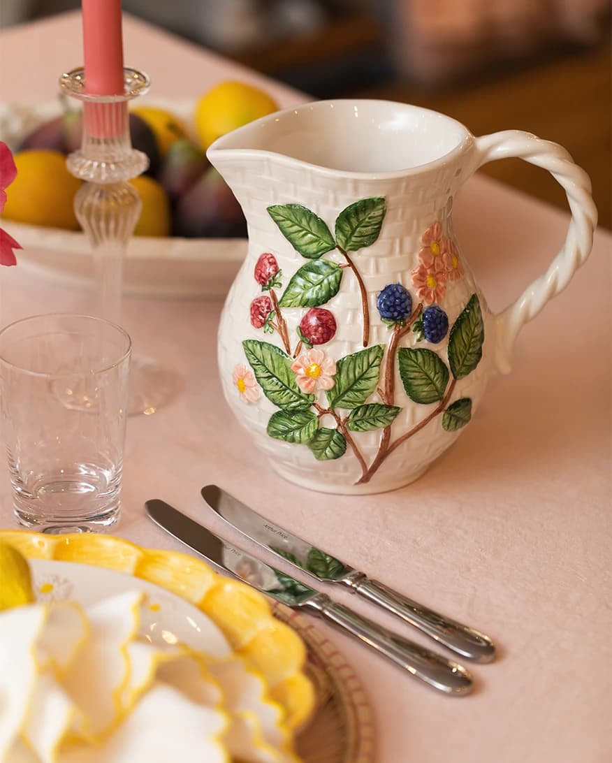 A luxury tableware wedding presents including handpainted plates and jug with fruit motif are arranged on a pink tablecloth