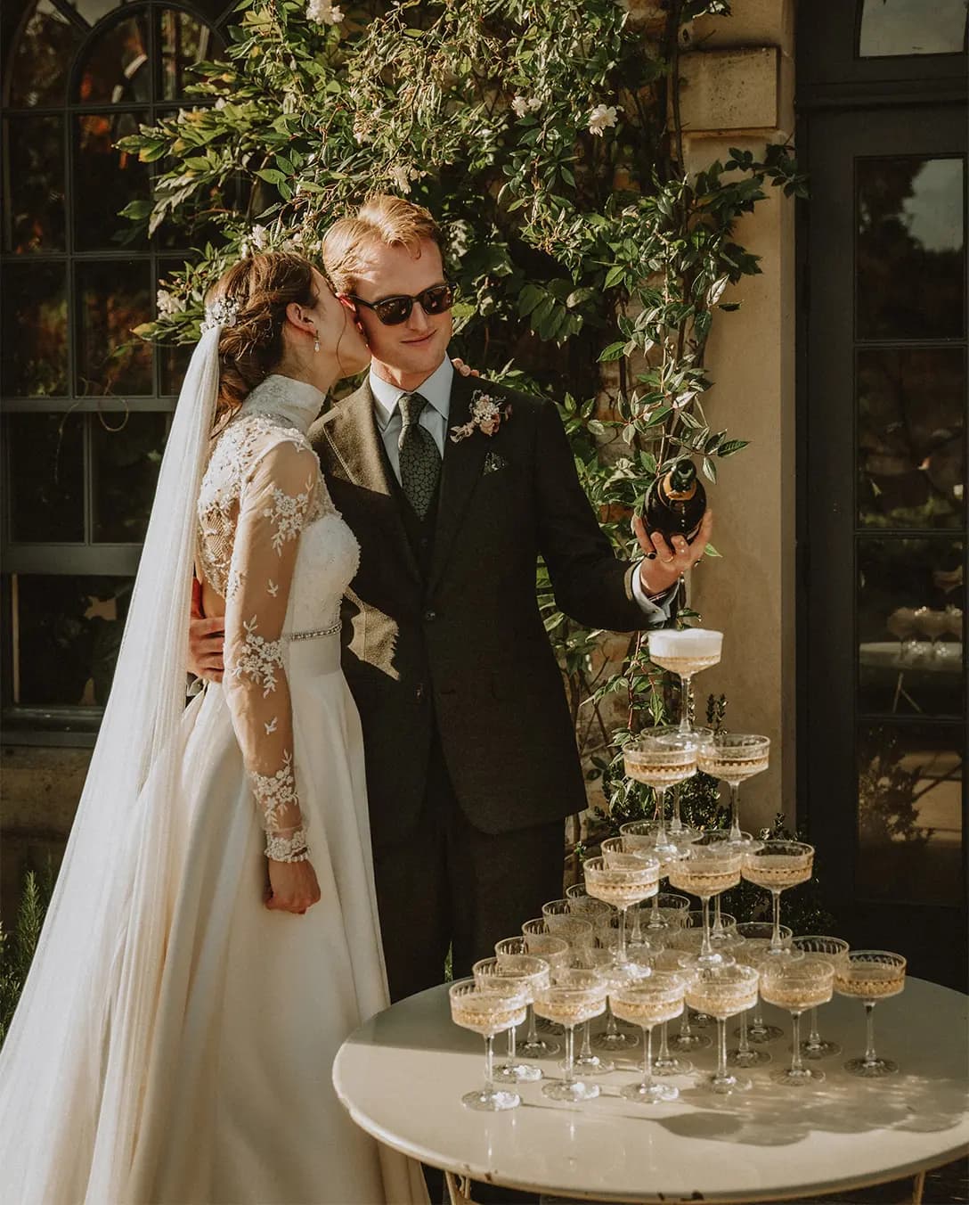 Bride and groom pour champagne over a tower made of coupe glasses.