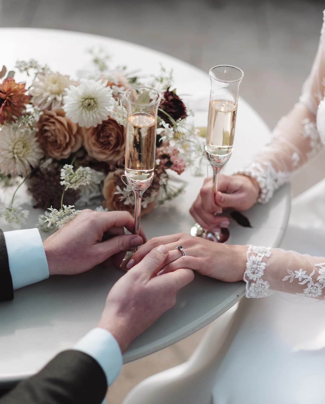 A close up of groom and bride holding hands with champagne on their wedding day