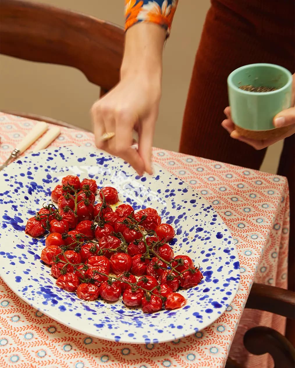 A hand sprinkles salt over food served in the platter with splatter design.