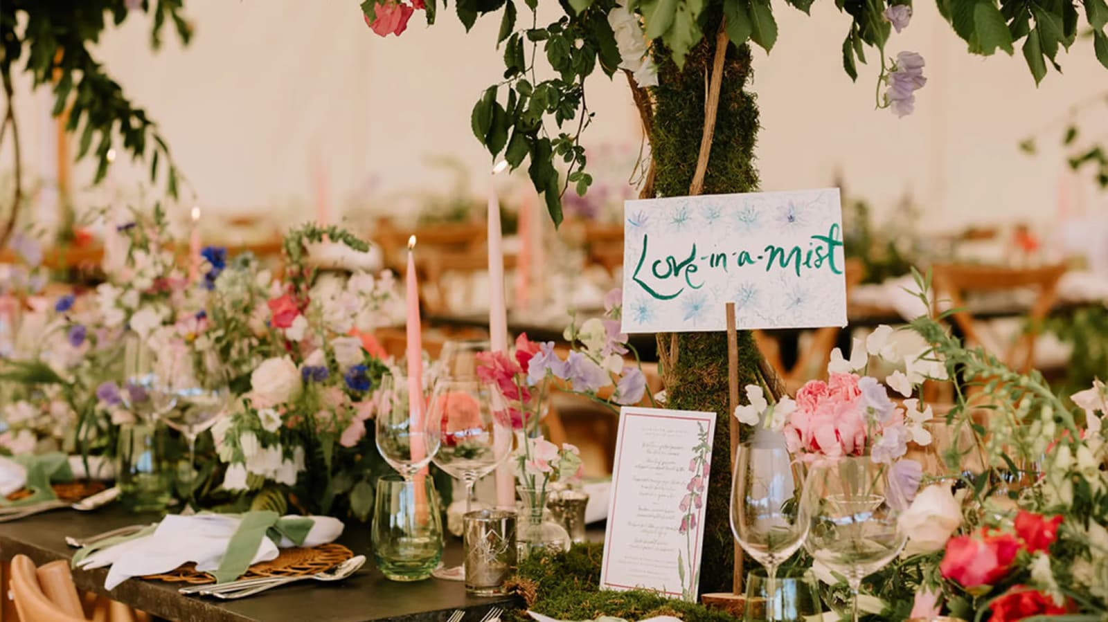 A hand-painted seating sign is placed on a wedding table with colourful flower arrangements.