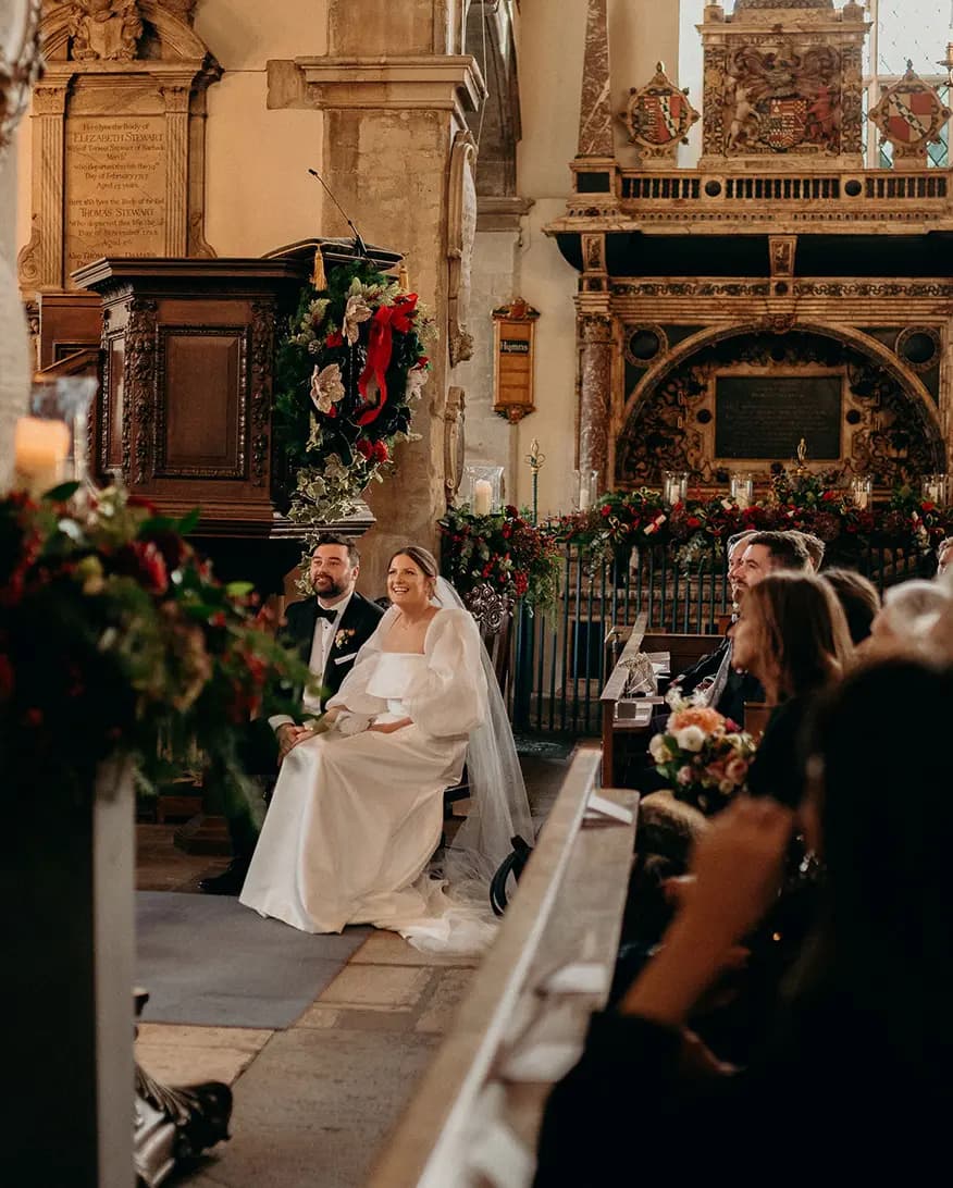 Bride and groom sit in church, listening to the wedding reading