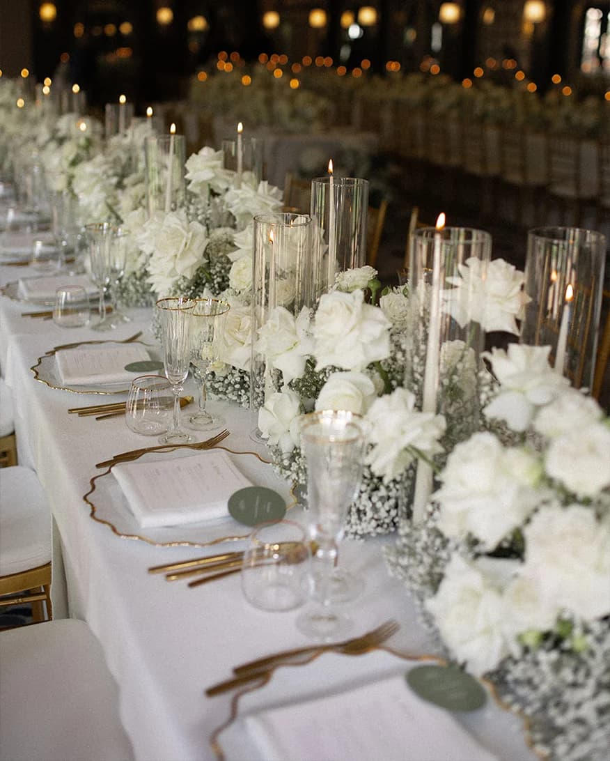 Luxury wedding table decor features white roses, candles in glass vases and luxury tableware