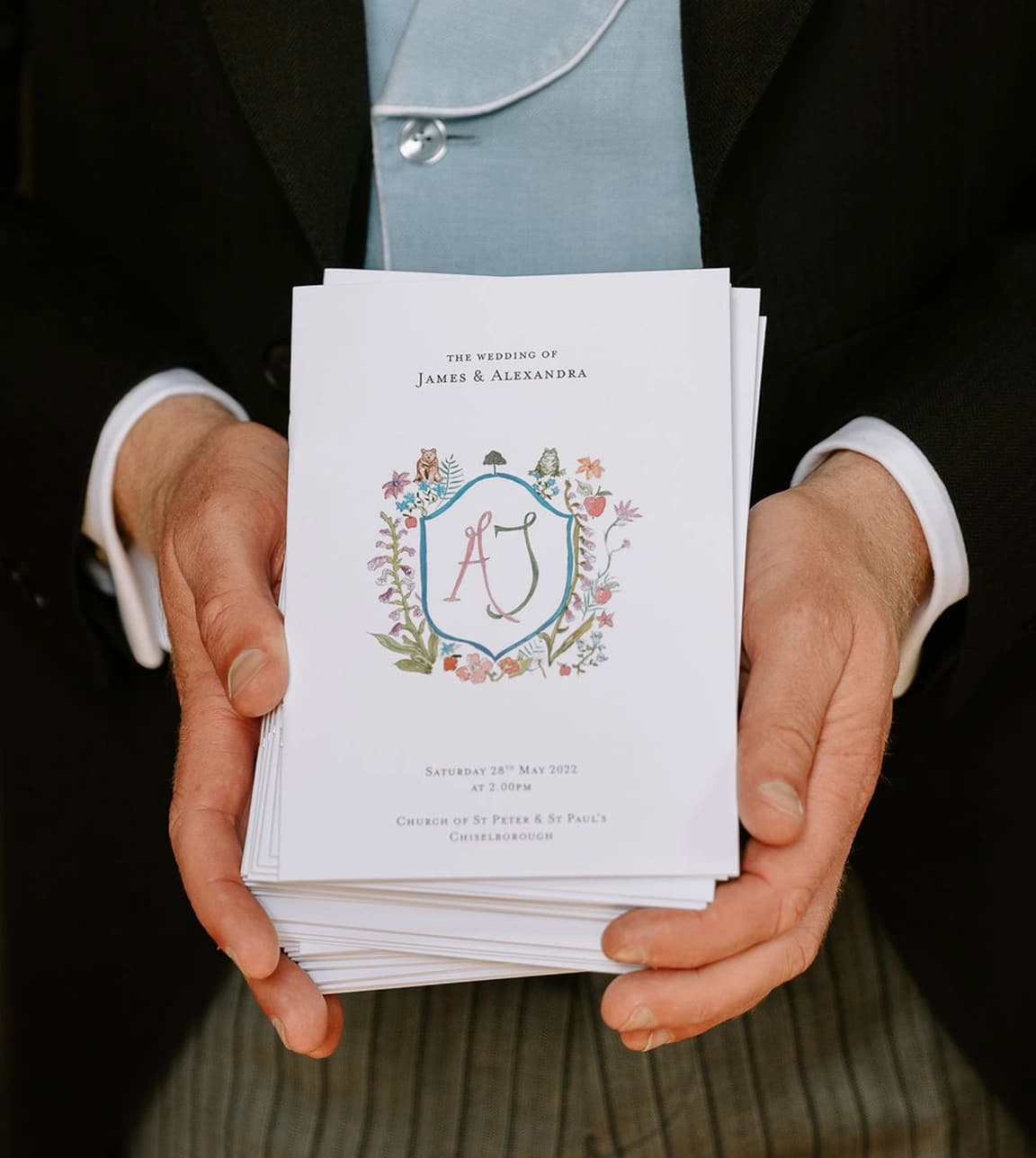 English groom in morning suit and blue waistcoat holds illustrated wedding invites