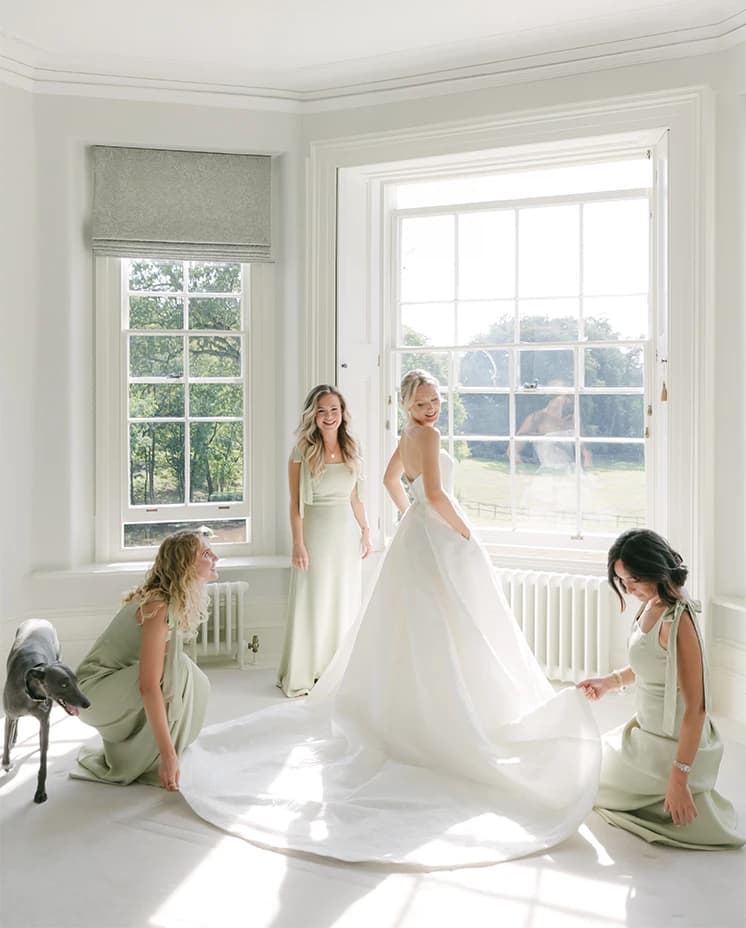 Bridesmaids help bride to get ready in the bridal suite of the manor house.