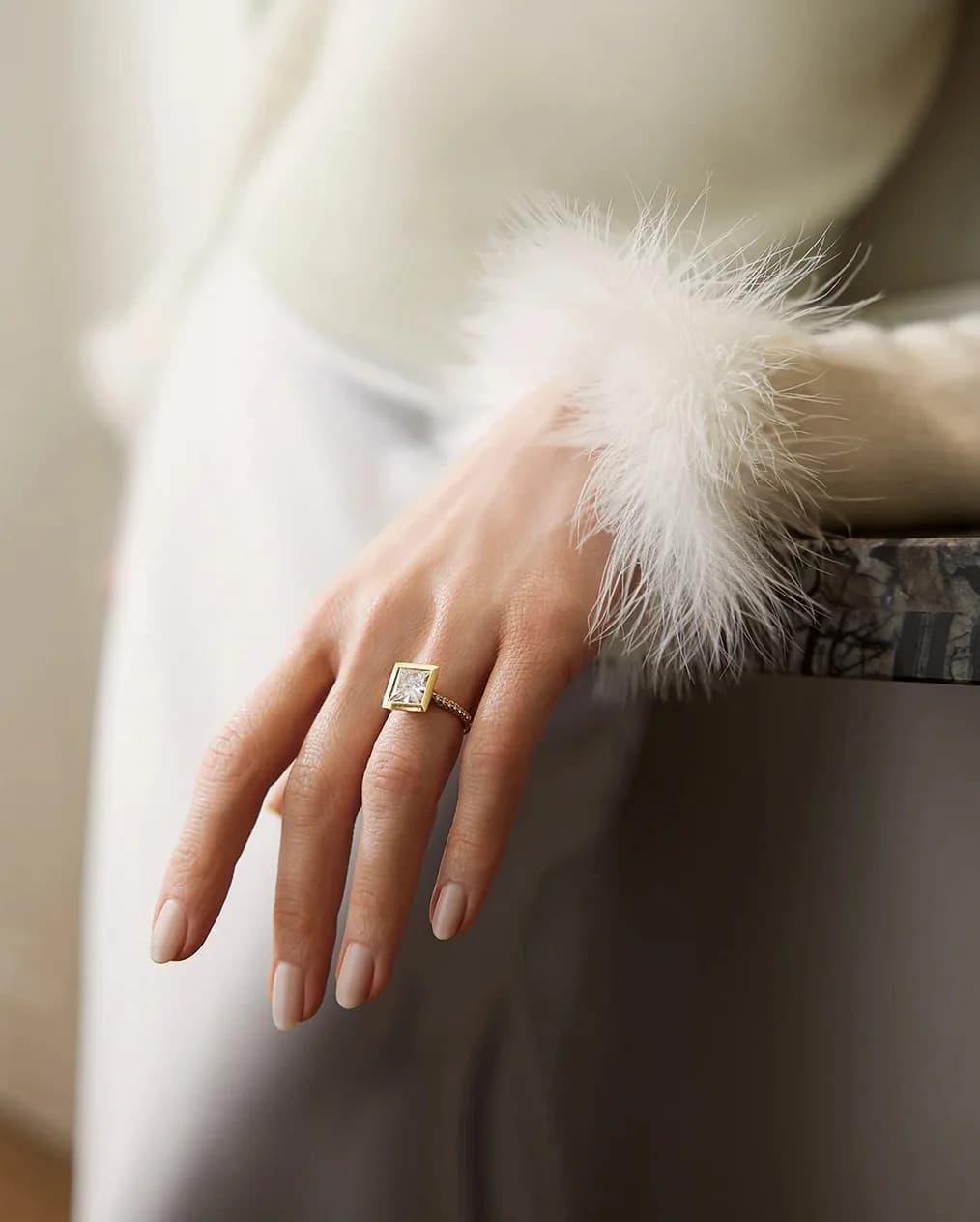A hand in sleek white sleeve, wearing Boodles princess cut yellow gold diamond ring