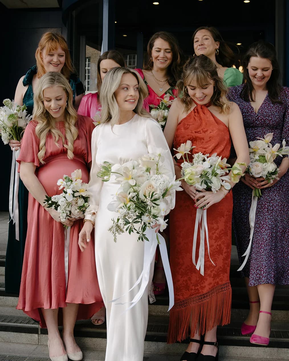 Bride with bridesmaids in mismatched dresses stand on stairs outside Marylebone Town Hall