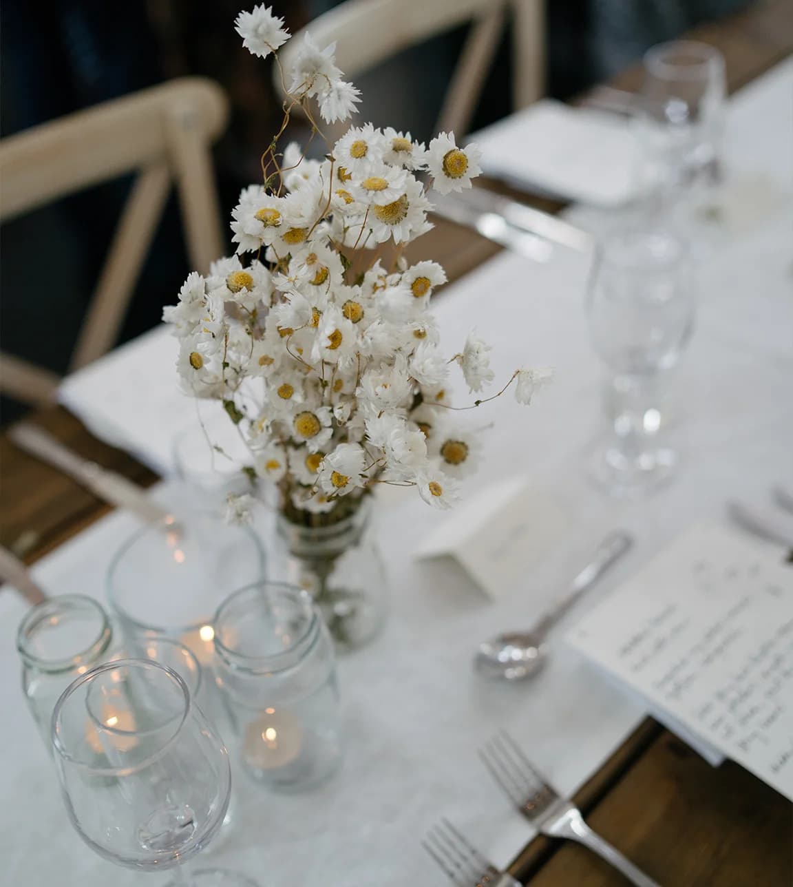 A simple wedding table décor featuring delicate bouquet of daisies, white table linen and handwritten wedding menu