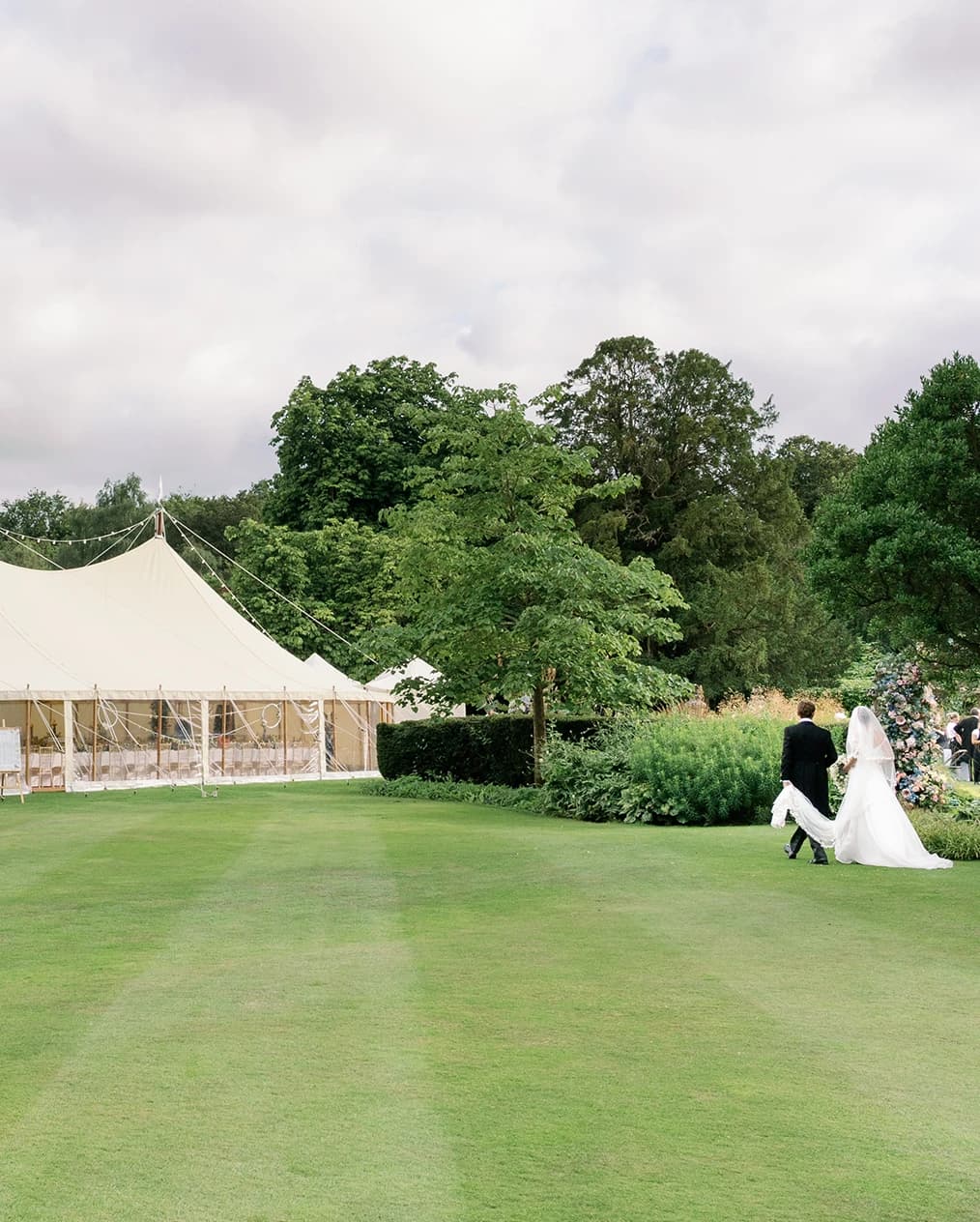 Bride and groom walks towards marquee in English garden