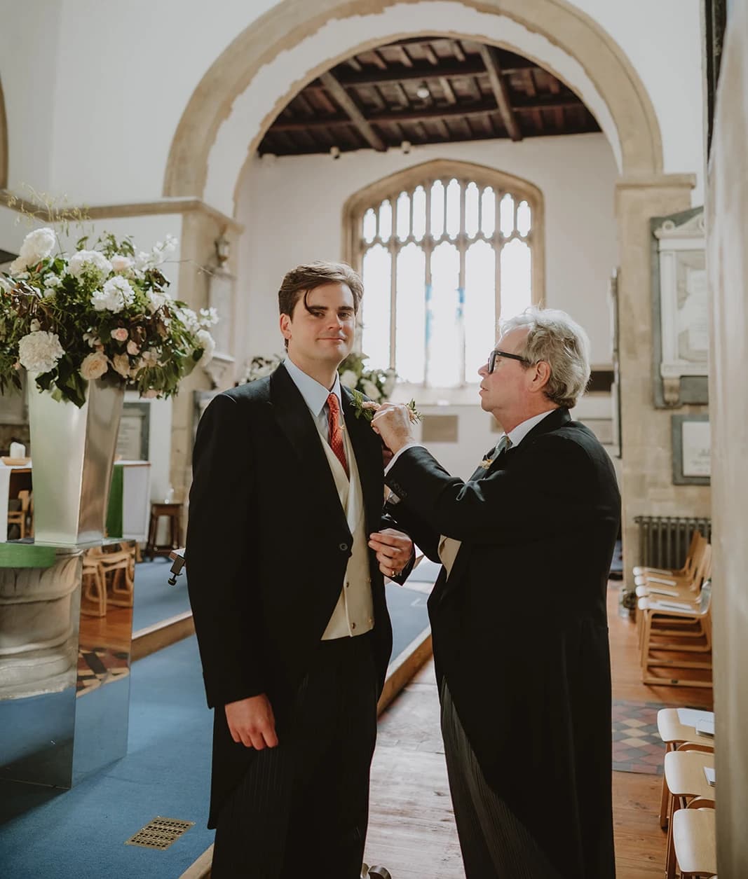 Groom in a morning suit having his flower buttonhole adjusted before the ceremony