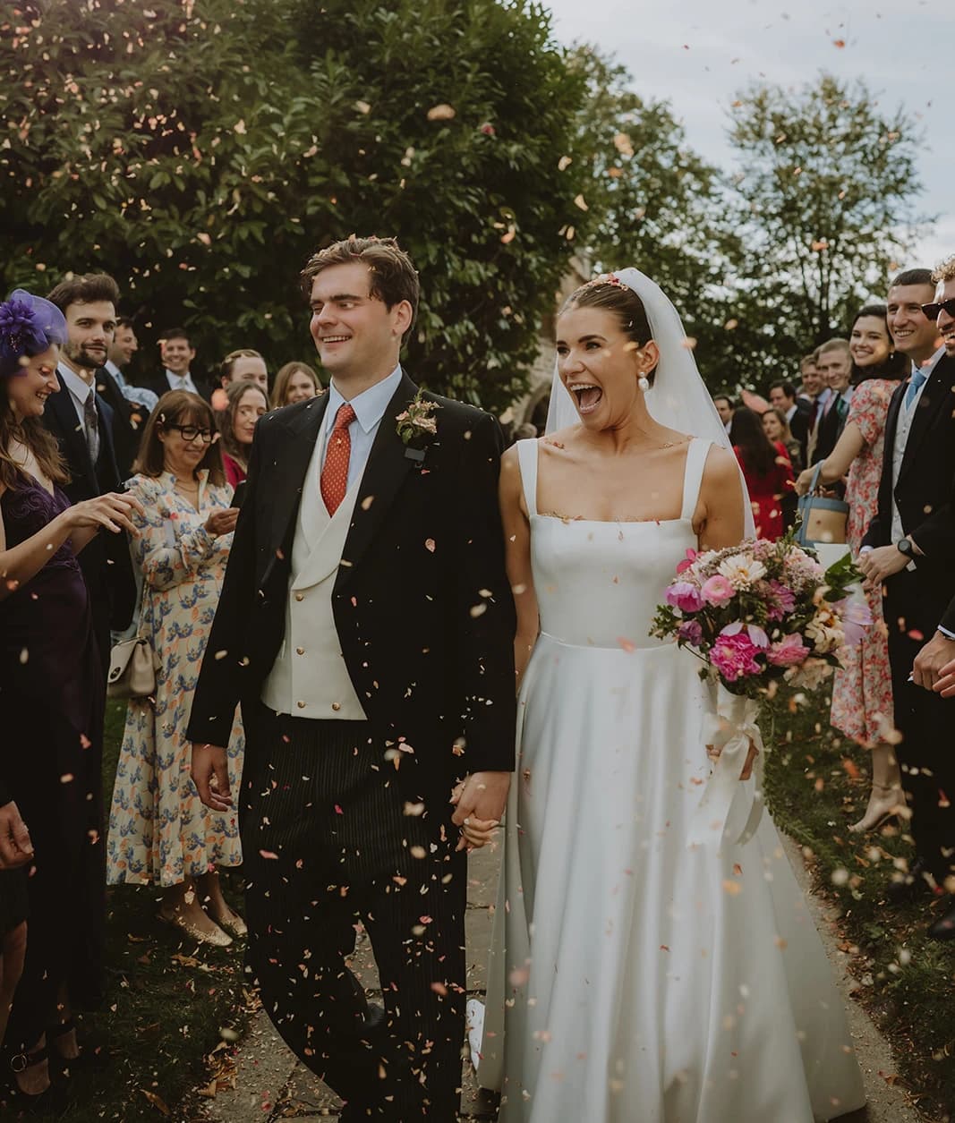 Bride laughing in delight as confetti falls outside St Edburg's Church