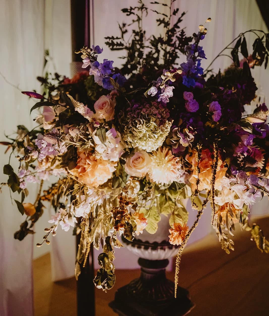 Purple, pink and peach floral urn arrangement lit up in the marquee at night