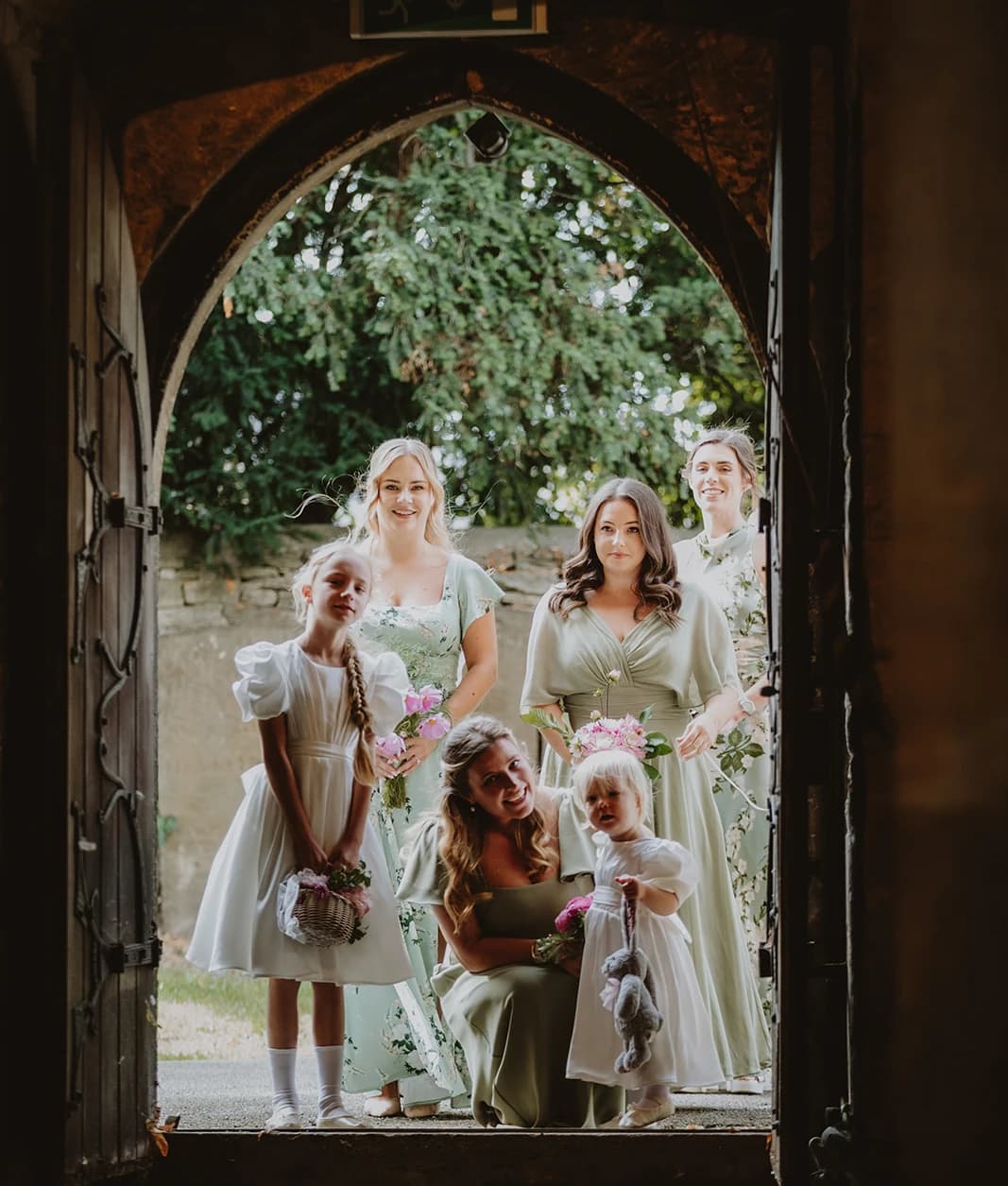 Bridesmaids in sage dresses and little flower girls in white waiting at the church door