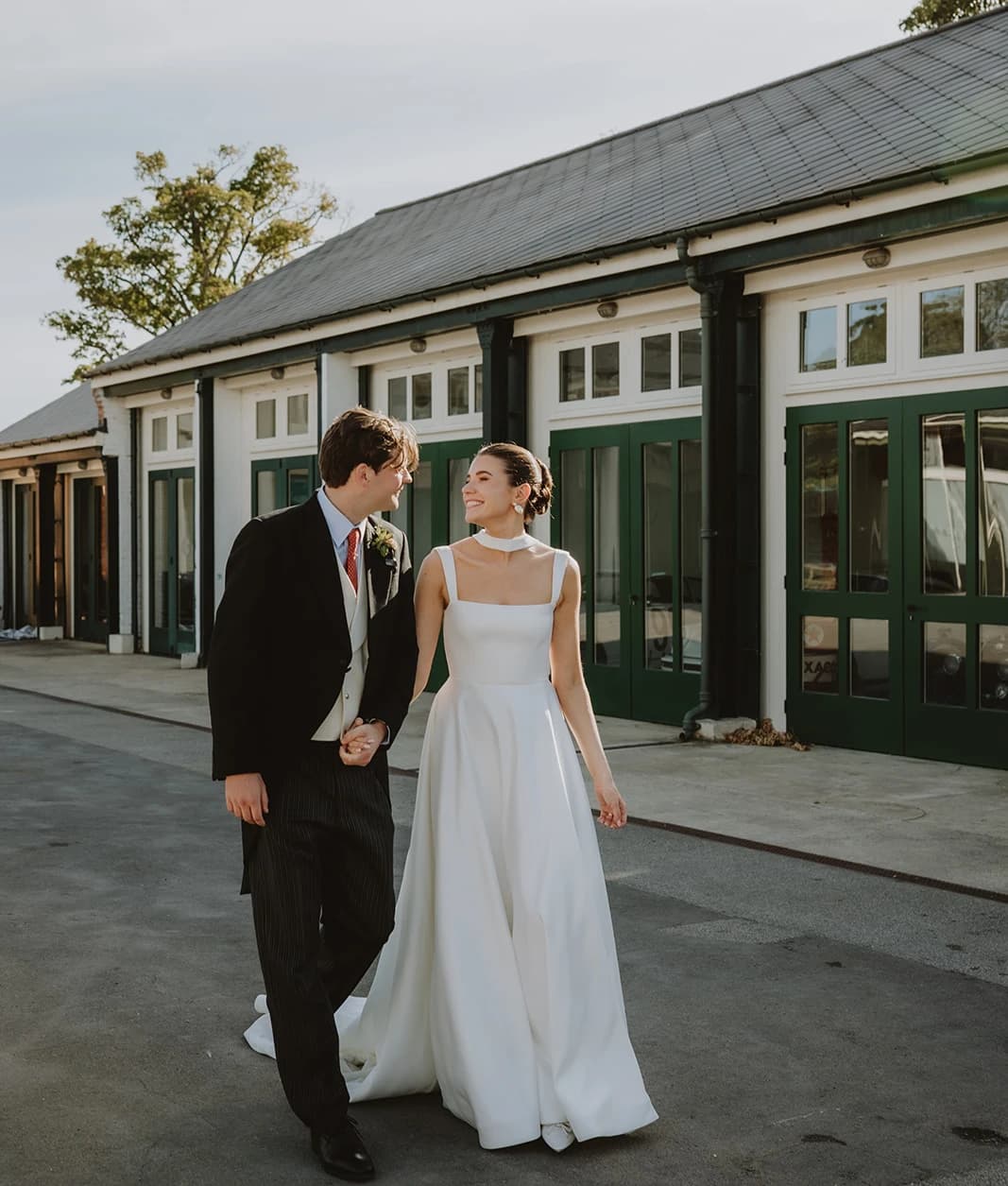 Bride smiling at the groom as they walk past the green-doored hangars
