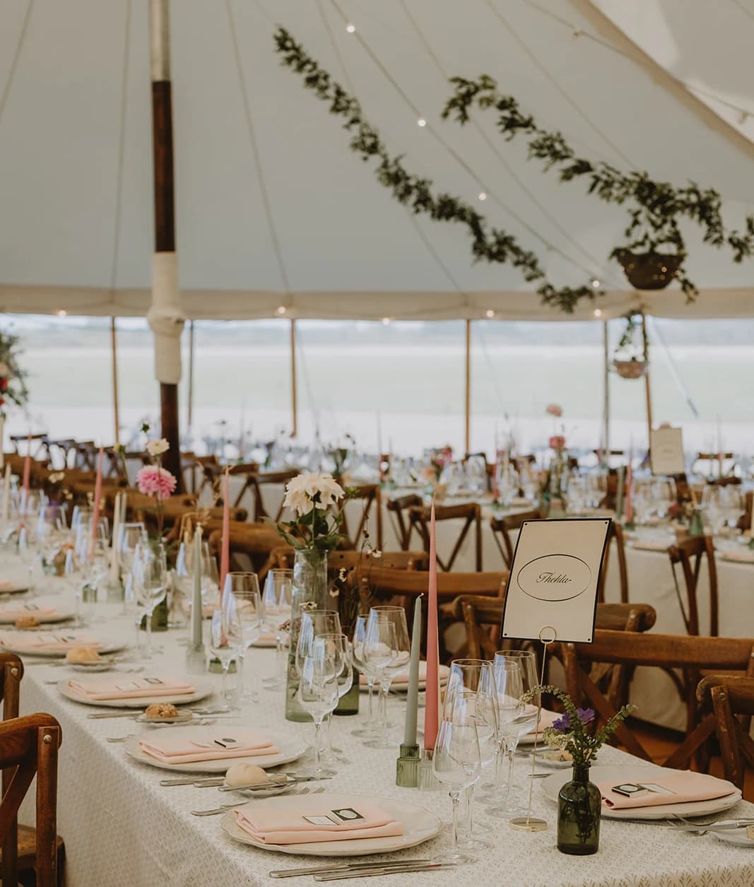 Marquee tables with table name cards, pink candles and foliage garlands overhead