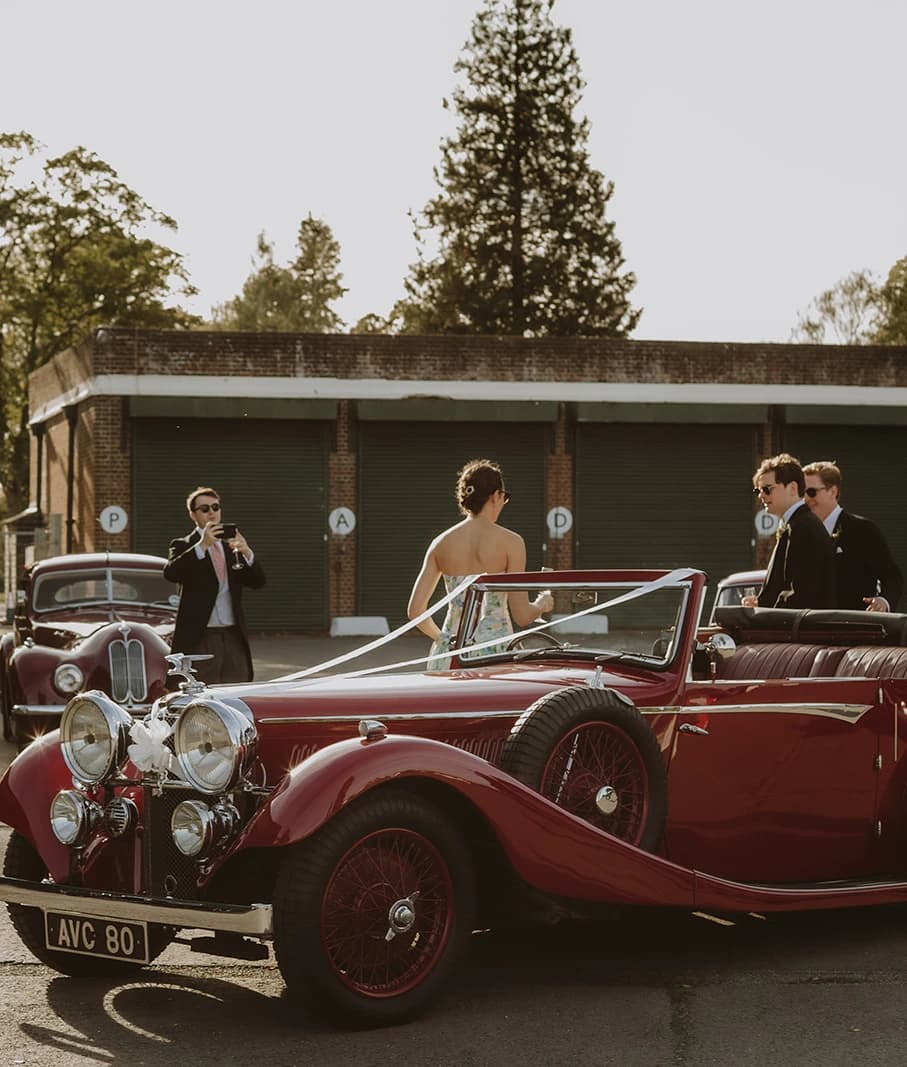Red vintage Alvis and classic cars lined up outside a hangar at Bicester Motion